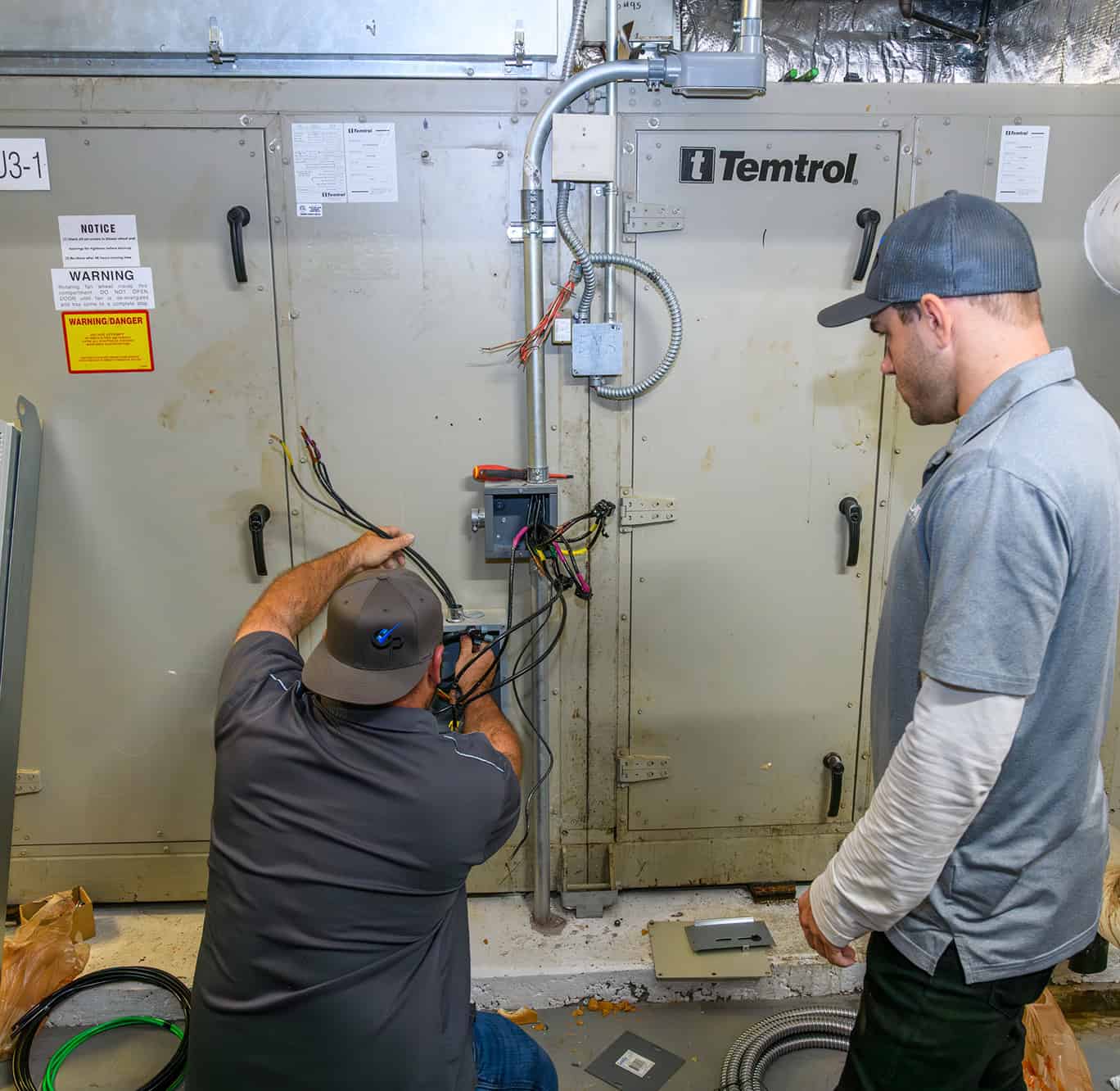 HVAC technician performing maintenance on commercial HVAC system with electrical wiring and control.