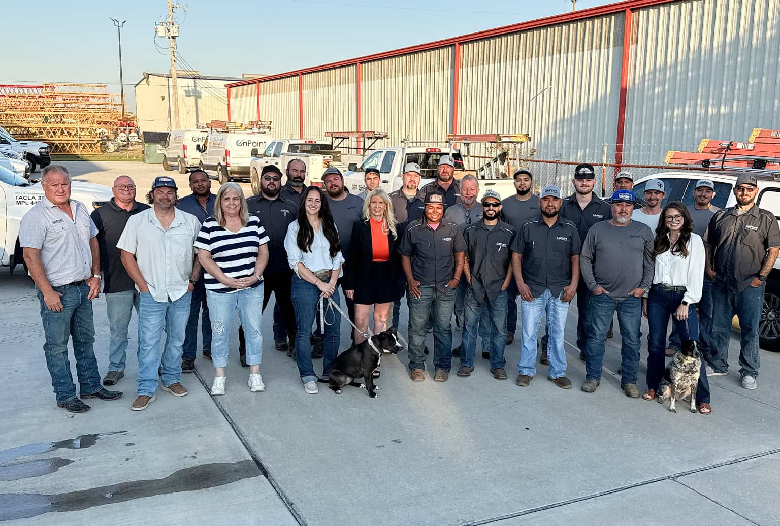 OnPoint Mechanical team group photo outdoors with employees and dogs, industrial background, sunny d.